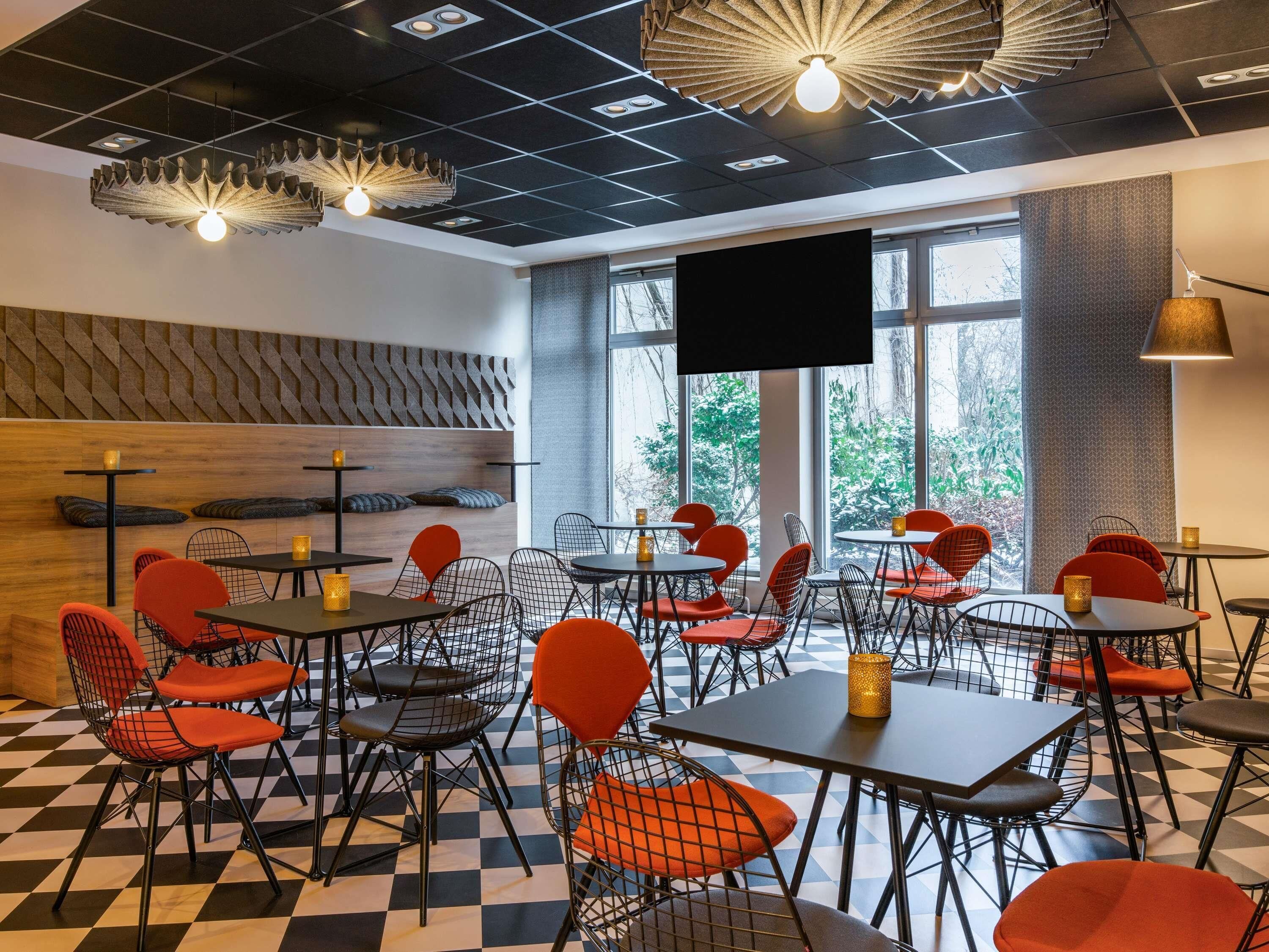 Un restaurante moderno con suelo a cuadros, sillas de malla metálica roja y negra, y una gran pantalla de televisión.