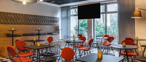 Un restaurante moderno con suelo a cuadros, sillas de malla metálica roja y negra, y una gran pantalla de televisión.