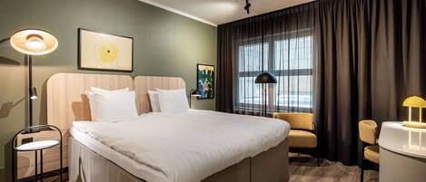 Una habitación de hotel con una cama grande, un escritorio, una silla, una lámpara y una ventana con cortinas.
