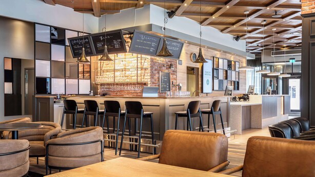A modern bar area with a brick wall, hanging lights, and a menu board. There are bar stools and a seating area with leather chairs. - Scandic Lahti City (Lahti)