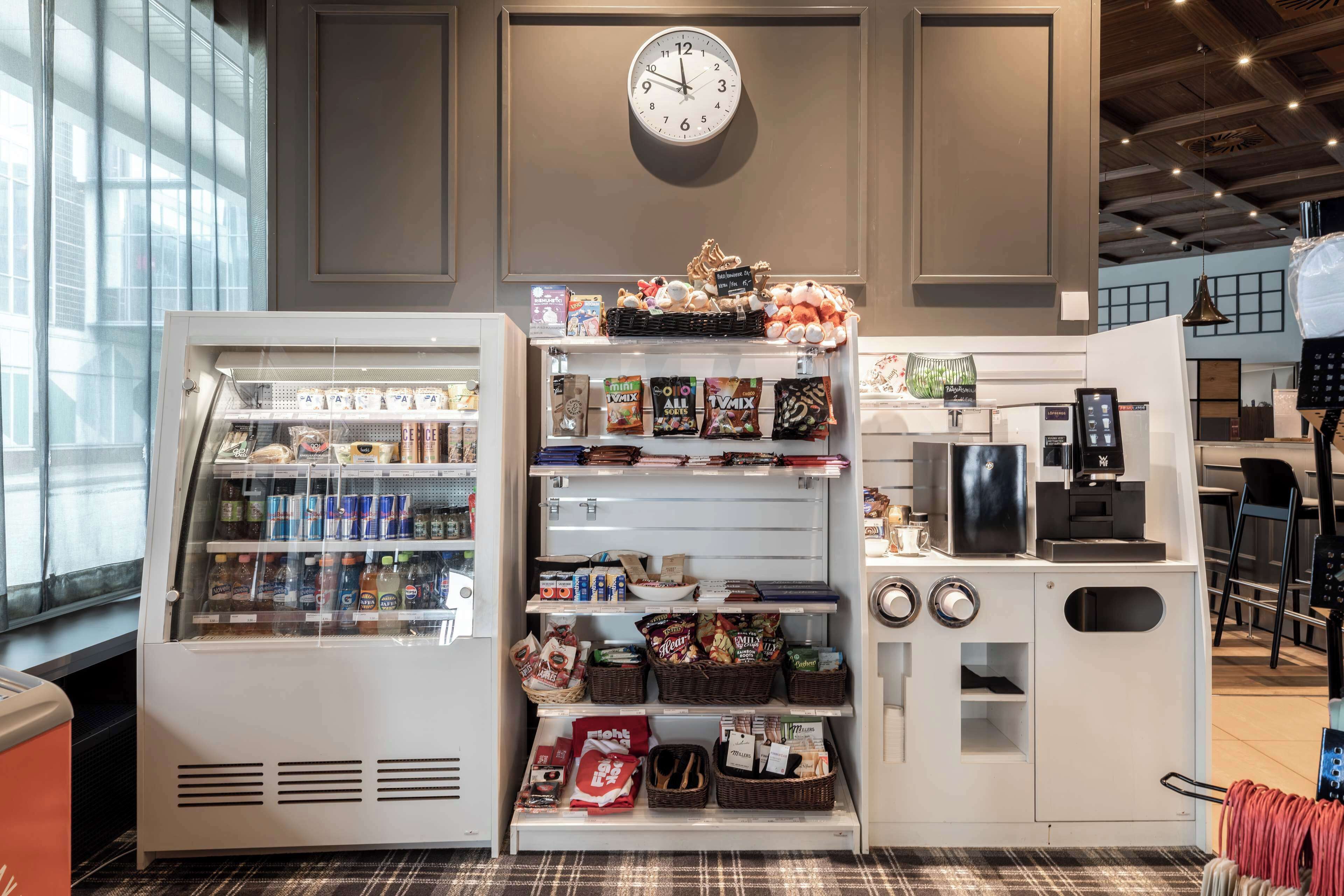 Quiosco de autoservicio con reloj, opciones de snacks y bebidas, y una máquina de café.