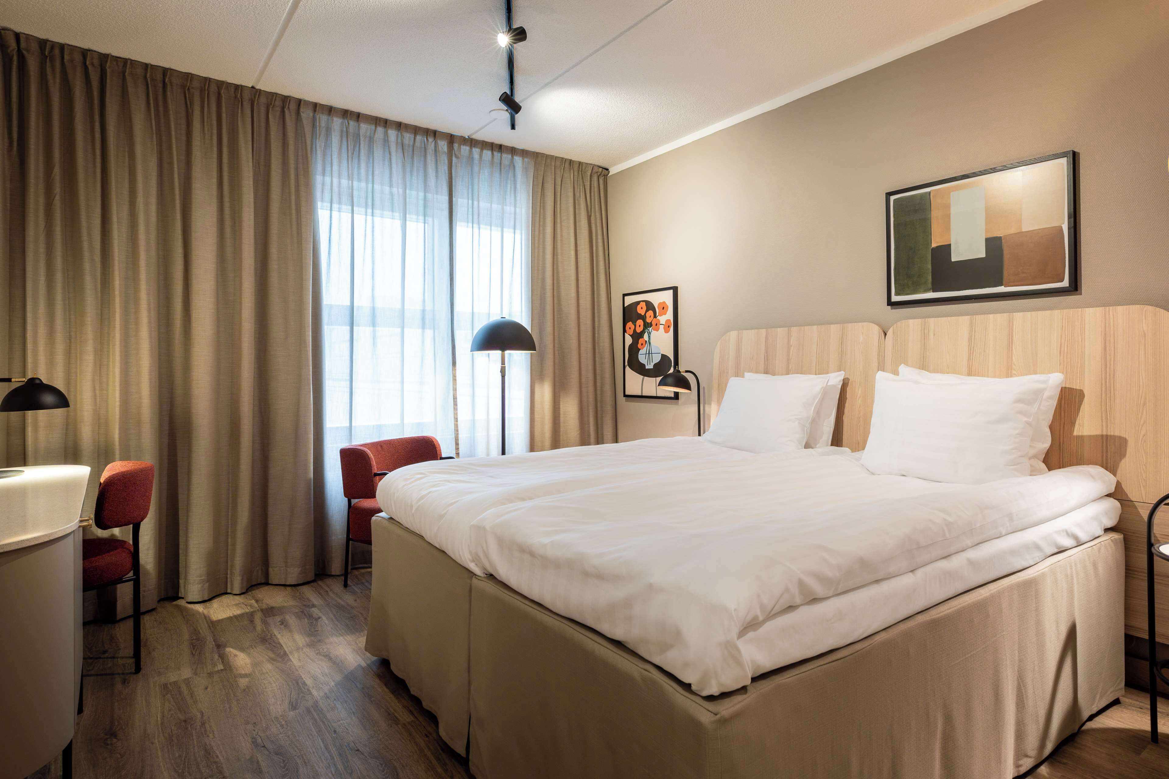 Ein Hotelzimmer mit einem großen Bett, einem Schreibtisch, einem Stuhl und einem fenster mit Vorhängen.