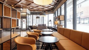 A modern interior with wooden ceiling beams, large windows, and a seating area with tables and chairs. - Scandic Lahti City (Lahti)