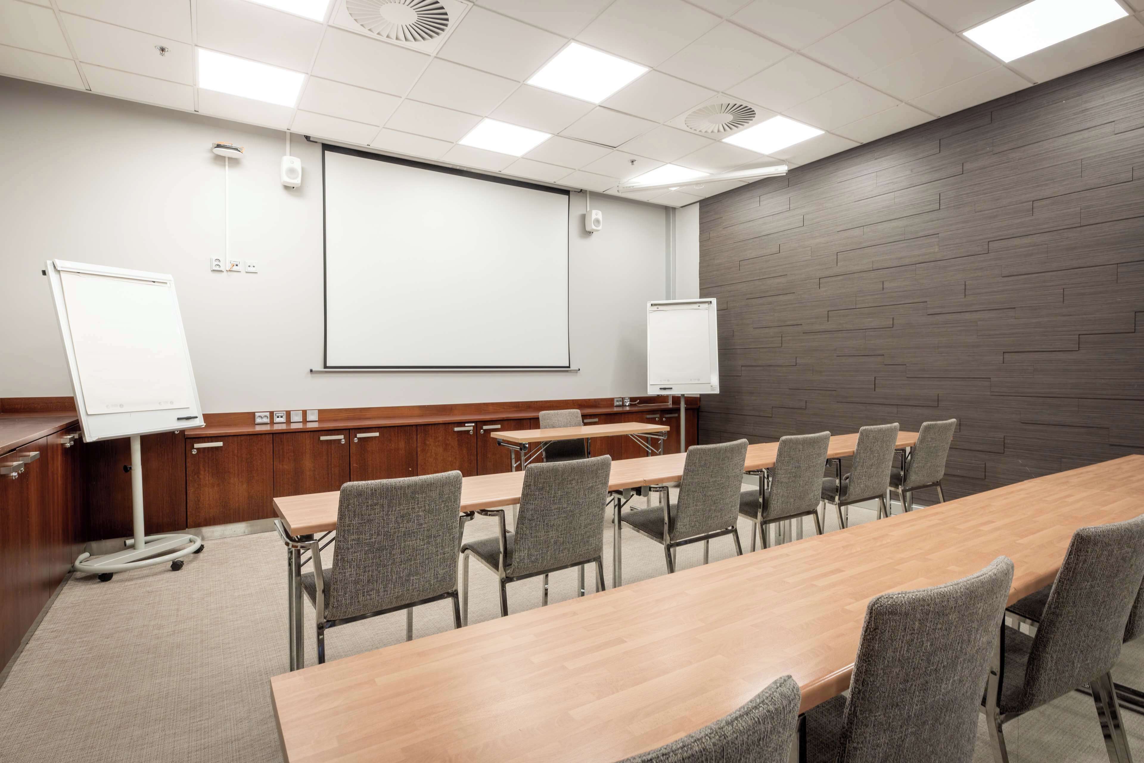 Een vergaderruimte met een lange tafel, meerdere stoelen, een whiteboard en een projectiescherm.