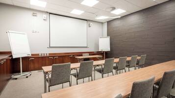 A conference room with a long table, multiple chairs, a whiteboard, and a projector screen.