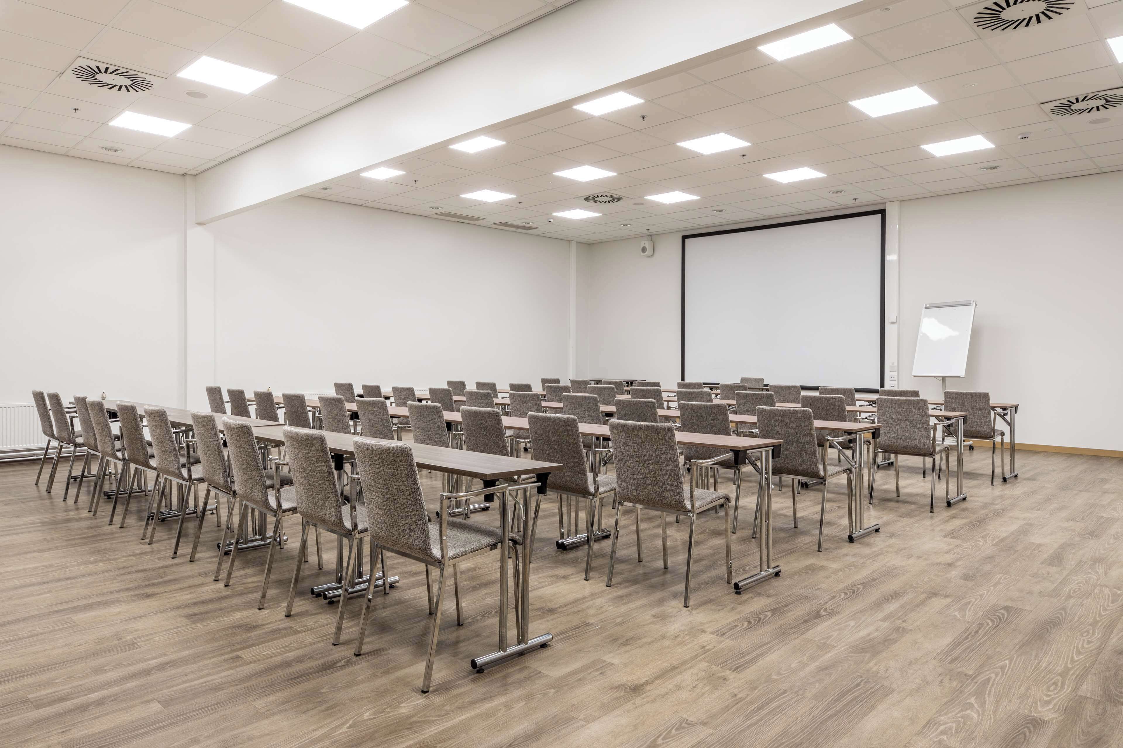 A conference room with rows of tables and chairs, a whiteboard, and a projector screen.