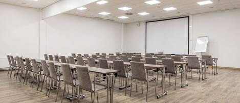 A conference room with rows of tables and chairs, a whiteboard, and a projector screen.