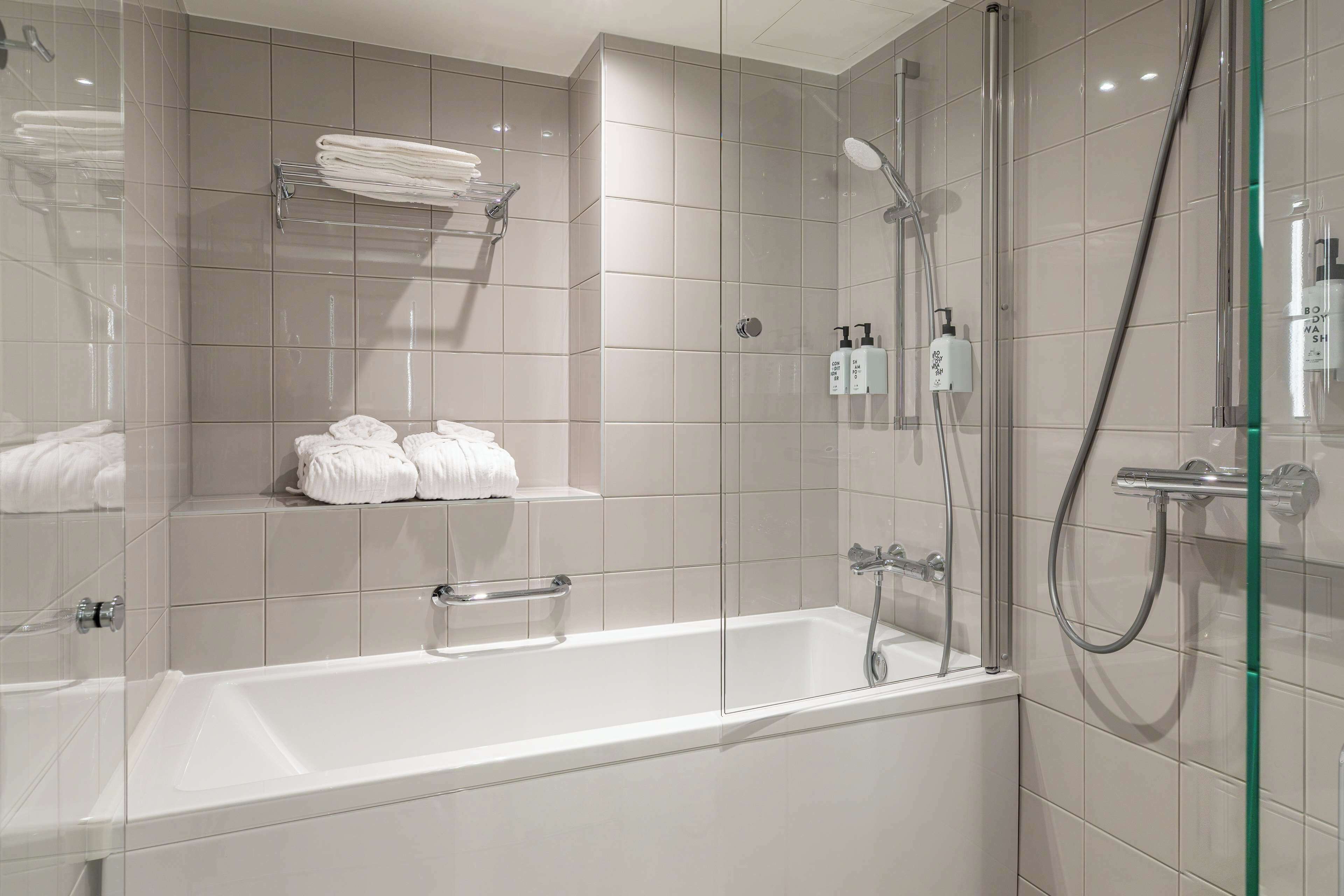 Un baño moderno con ducha de vidrio, una bañera blanca y toallas ordenadas en estantes.