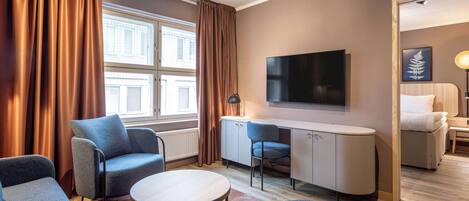 Habitación de hotel moderna con sofá, una mesa redonda, televisor montado en la pared y escritorio con silla.