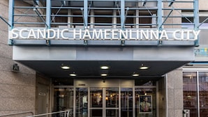 La entrada a Scandic Hämeenlinna City con un diseño moderno, que presenta un frente de vidrio y barandillas de metal.