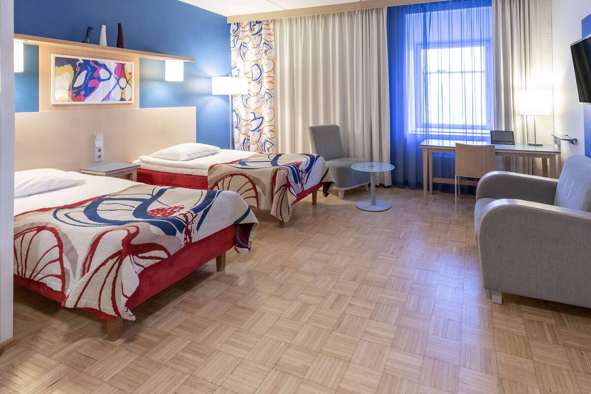 Habitació d'hotel amb dos llits, una taula, una cadira i un televisor.