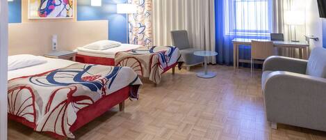 A hotel room with two beds, a desk, a chair, and a TV.