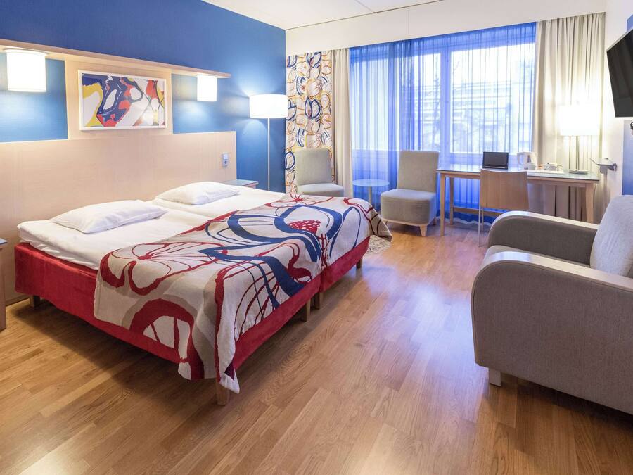 Ein Hotelzimmer mit einem großen Bett, einem Schreibtisch, einem Stuhl und einem Fernseher.