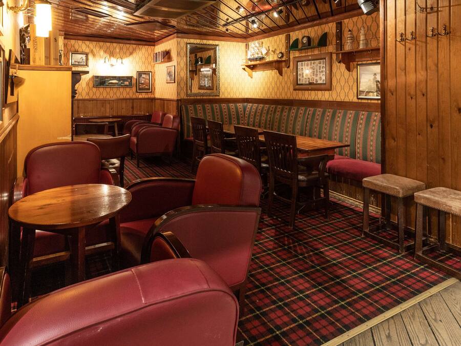 A cozy restaurant interior with wooden walls, plaid flooring, and red upholstered booths.