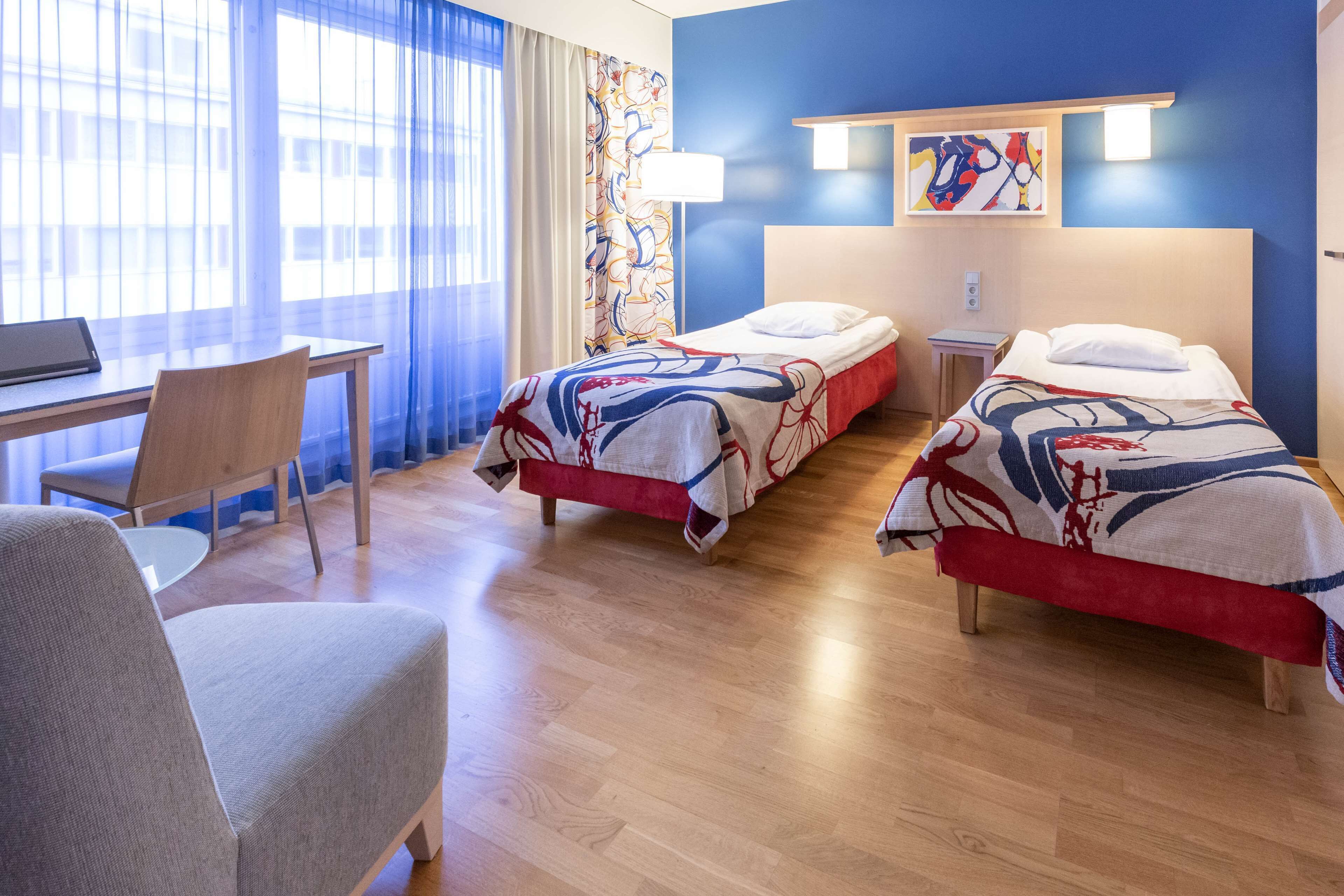 Ein Hotelzimmer mit zwei Betten, einem Schreibtisch und einem Stuhl.