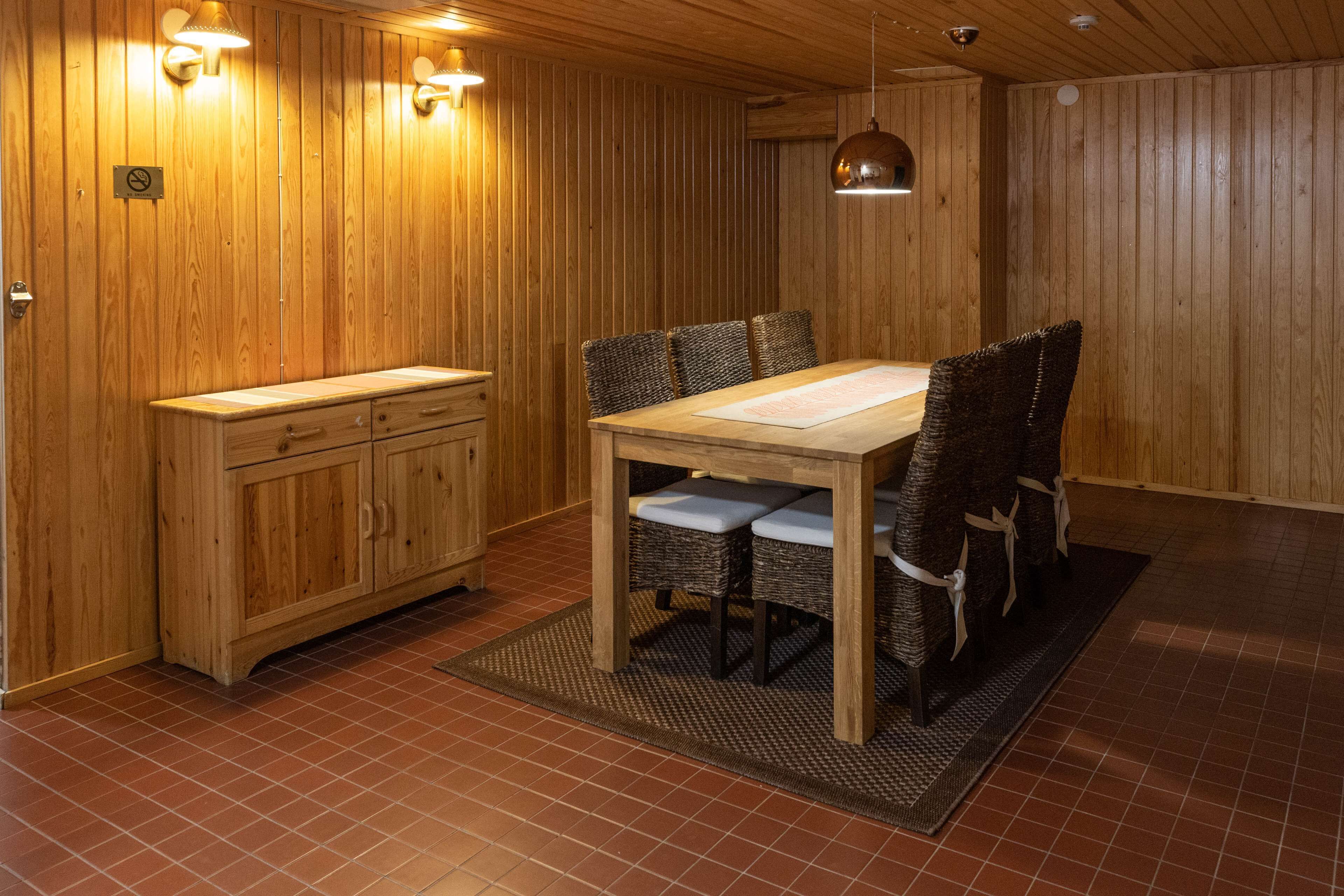 A wooden-paneled room with a dining table and chairs, a wooden cabinet, and a hanging pendant light.