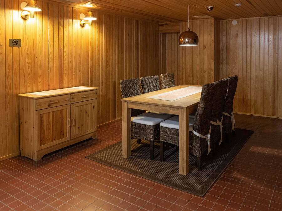 A wooden-paneled room with a dining table and chairs, a wooden cabinet, and a hanging pendant light.