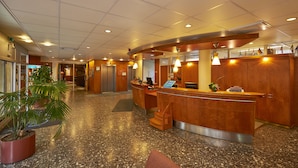Zona de recepción de hotel con un mostrador curvo, una planta en maceta y suelo de mármol.