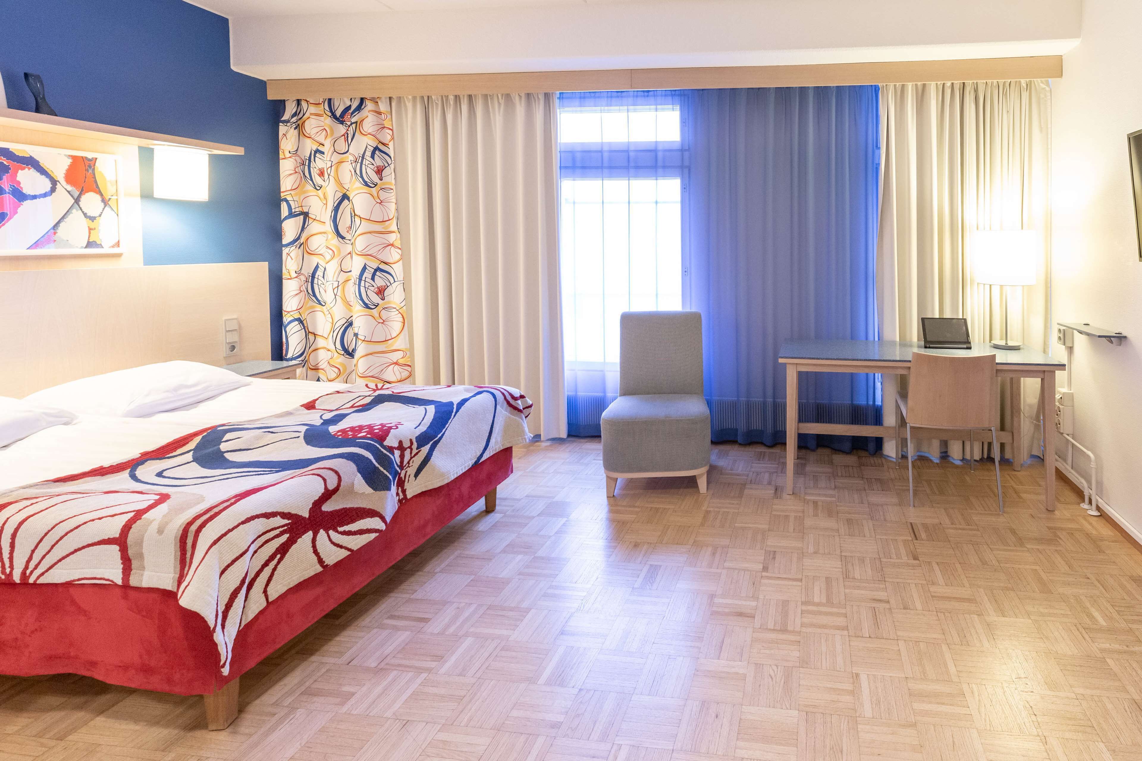 A hotel room with a bed, a desk, a chair, and a window with curtains.