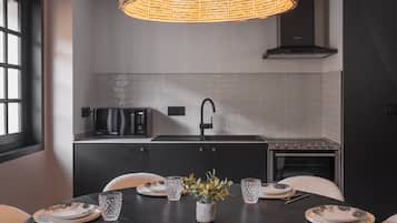 Cocina moderna con una mesa de comedor preparada para dos personas, con encimera negra, extractor de acero inoxidable y ventana que proporciona luz natural.