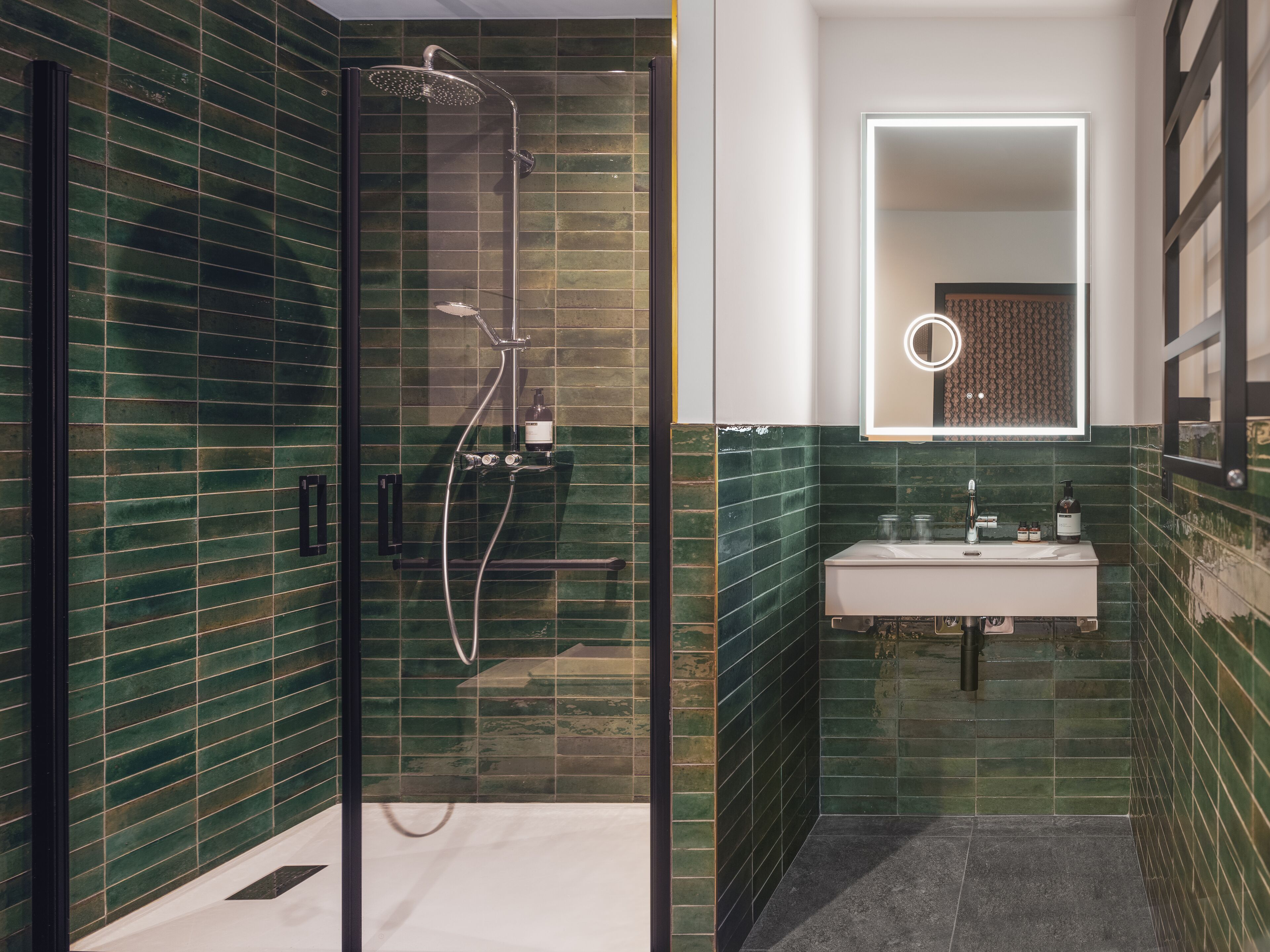 Une salle de bain moderne avec une douche à parois de verre, un lavabo blanc et des murs recouverts de carreaux verts.