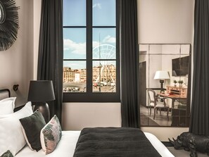 A hotel room with a bed, a desk, and a view of a Ferris wheel and buildings. - Maisons du Monde Hôtel & Suites - Marseille Vieux Port (Marseille)