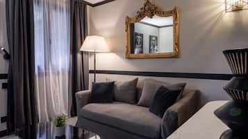 A modern hotel room with a grey sofa, a black coffee table, a floor lamp, a large mirror, and a decorative vase.