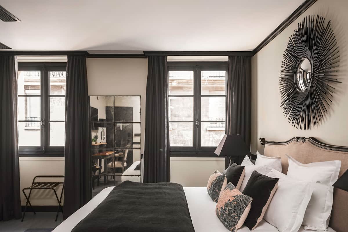 A hotel room with a large bed, a desk with a chair, a mirror, and a view through the window.