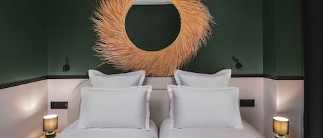 A bed with white bedding, two bedside lamps, and a large circular mirror with a textured frame.