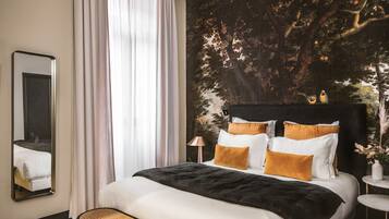 Een moderne slaapkamer met een groot bed, een spiegel, een raam met dunne gordijnen en een muurschildering van een boom.
