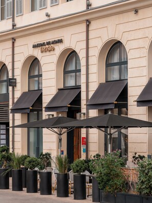A building with arched windows and awnings, outdoor seating with black umbrellas, and potted plants. - Maisons du Monde Hôtel & Suites - Marseille Vieux Port (Marseille)