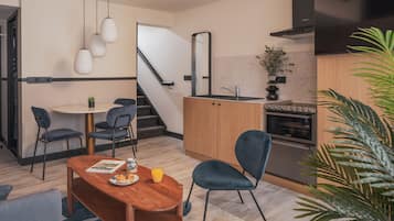 Een moderne keuken met een inbouwoven, een eethoek met een houten tafel en stoelen, en een trap die naar een ander niveau leidt.