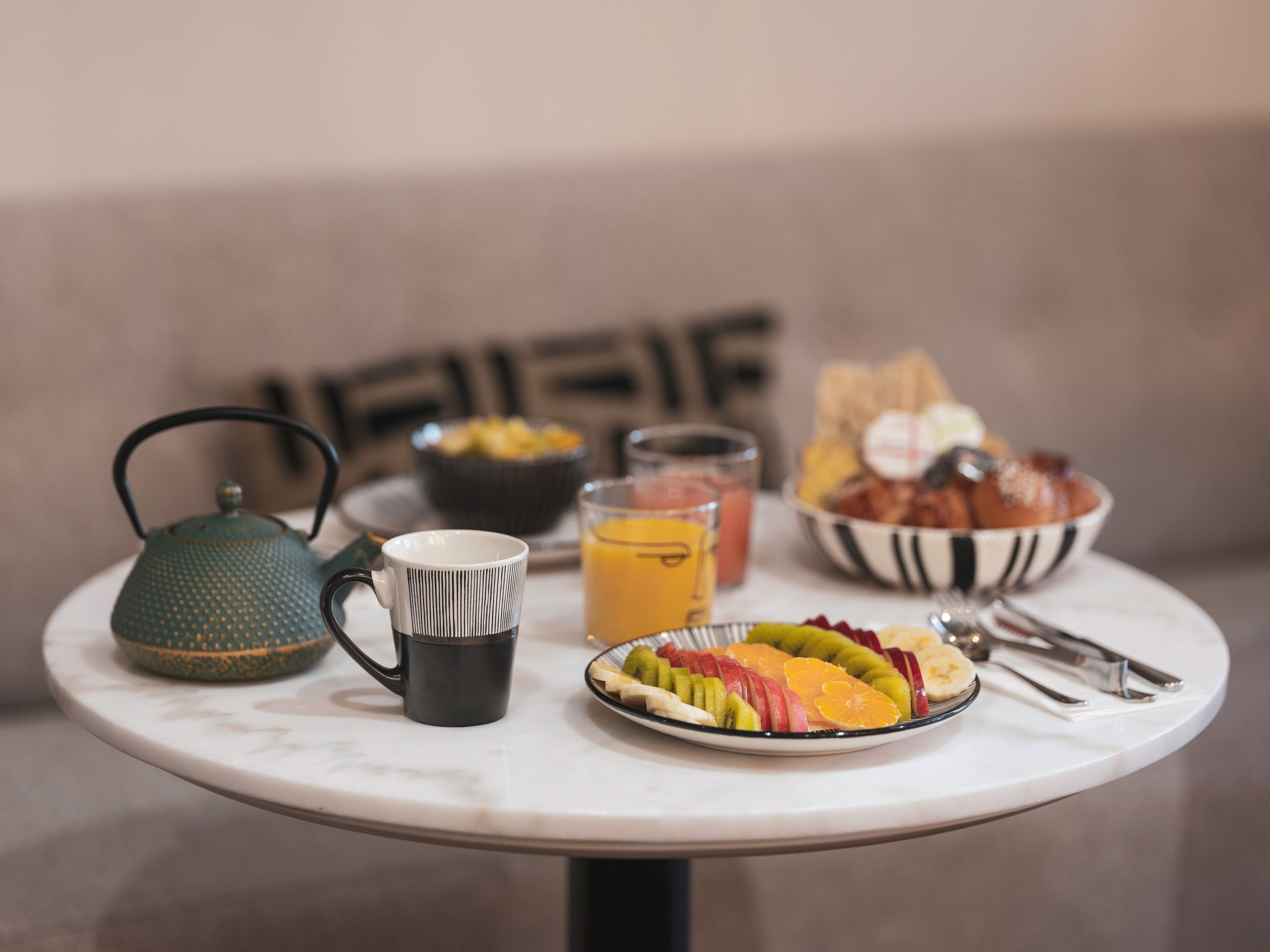 A breakfast table with a teapot, mug, fruit, juice, and a bowl of eggs.