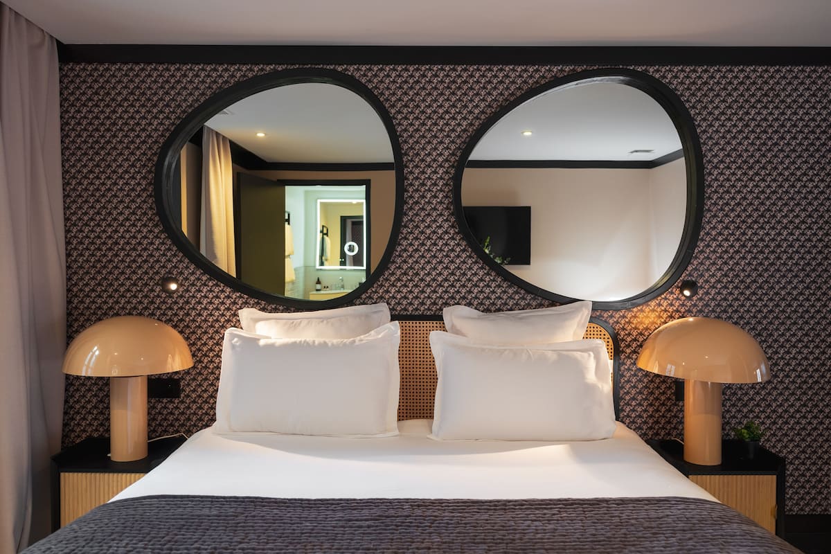 A hotel room with a large bed, two bedside lamps, and two round mirrors on the wall.