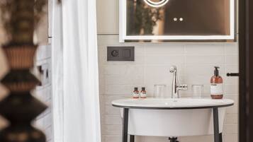 A bathroom with a round white sink, a mirror with a light, and a towel on a small shelf.