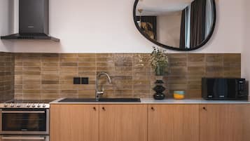 Una cocina moderna con horno empotrado, campana extractora de acero inoxidable, pileta, microondas y un florero decorativo con flores.