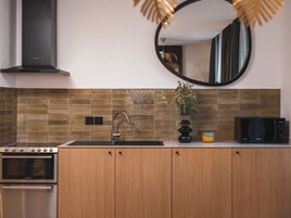 Una cocina moderna con horno empotrado, campana extractora de acero inoxidable, pileta, microondas y un florero decorativo con flores.
