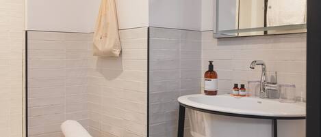 A modern bathroom with a white sink, mirror, and a wooden stool with towels.