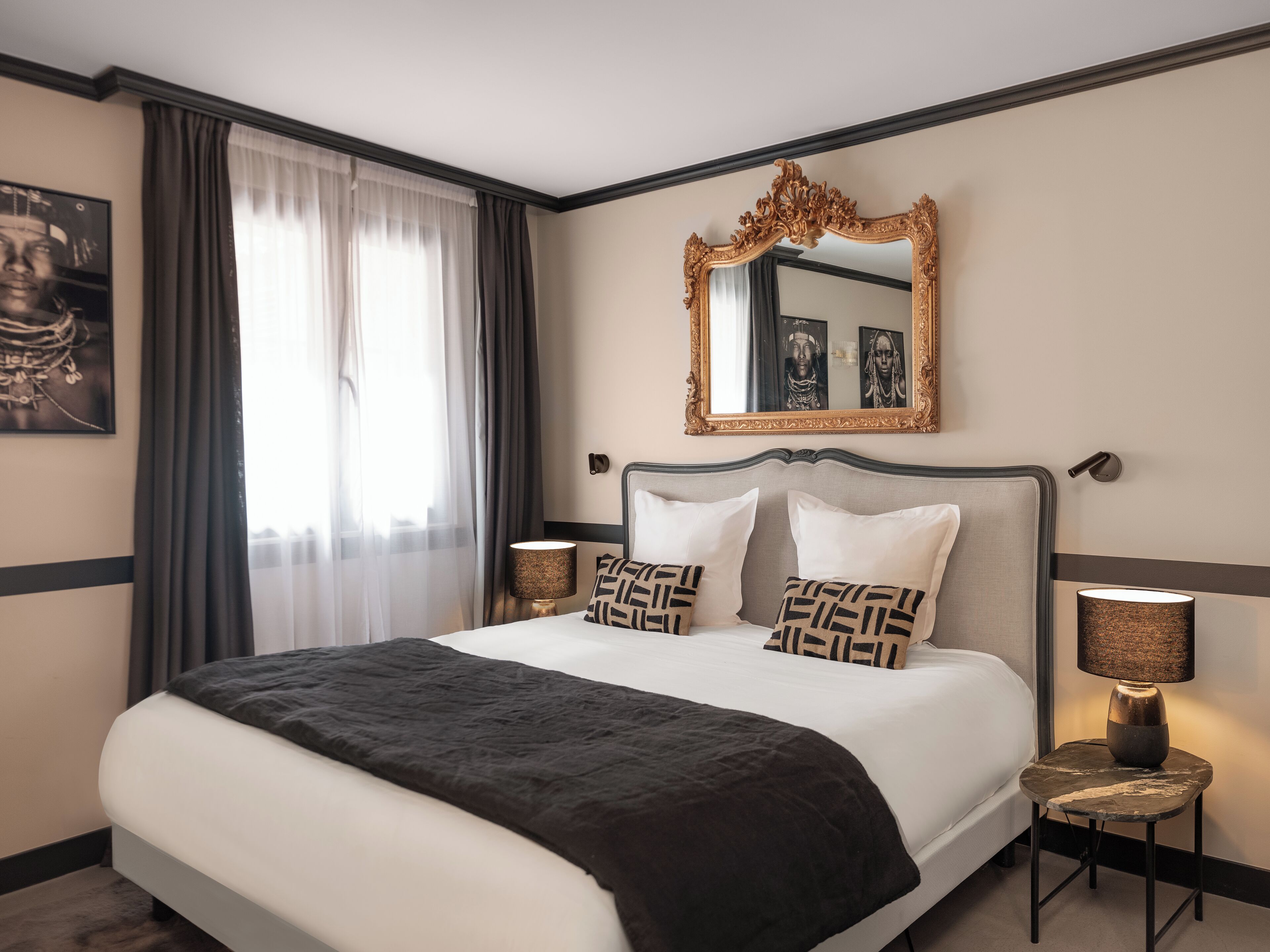 A hotel room with a large bed, two bedside tables with lamps, a mirror, and a window with curtains.