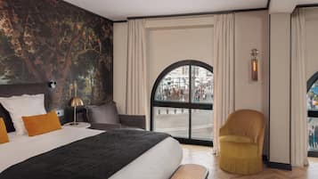 Una habitación de hotel moderna con una cama grande, un banco y vistas a una calle concurrida, además de un mural en la pared.