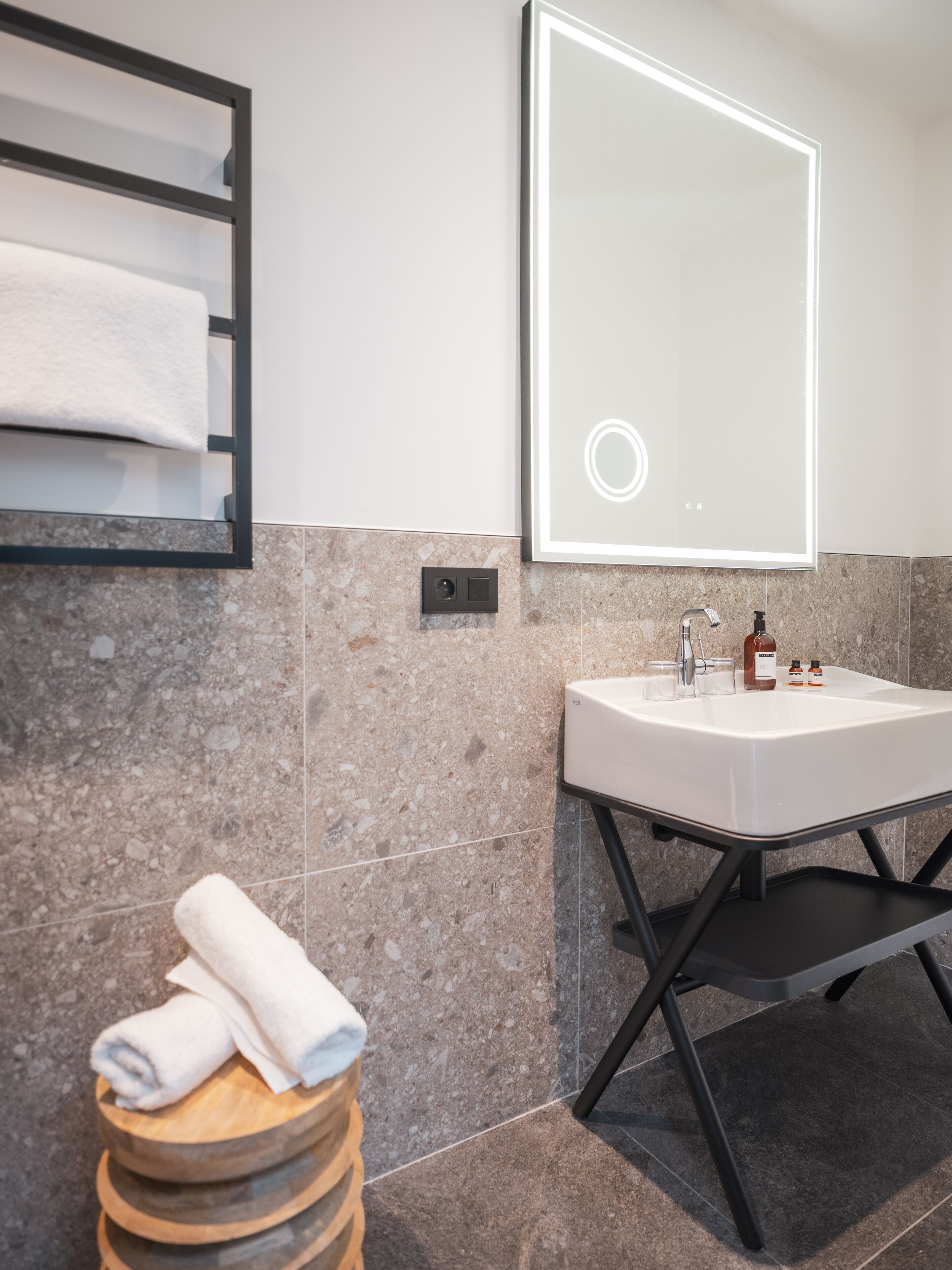 Un baño moderno con un lavamanos blanco, un espejo grande y un perchero para toallas.