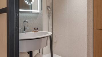 Un baño moderno con ducha de vidrio, lavamanos blanco y espejo con luz circular.