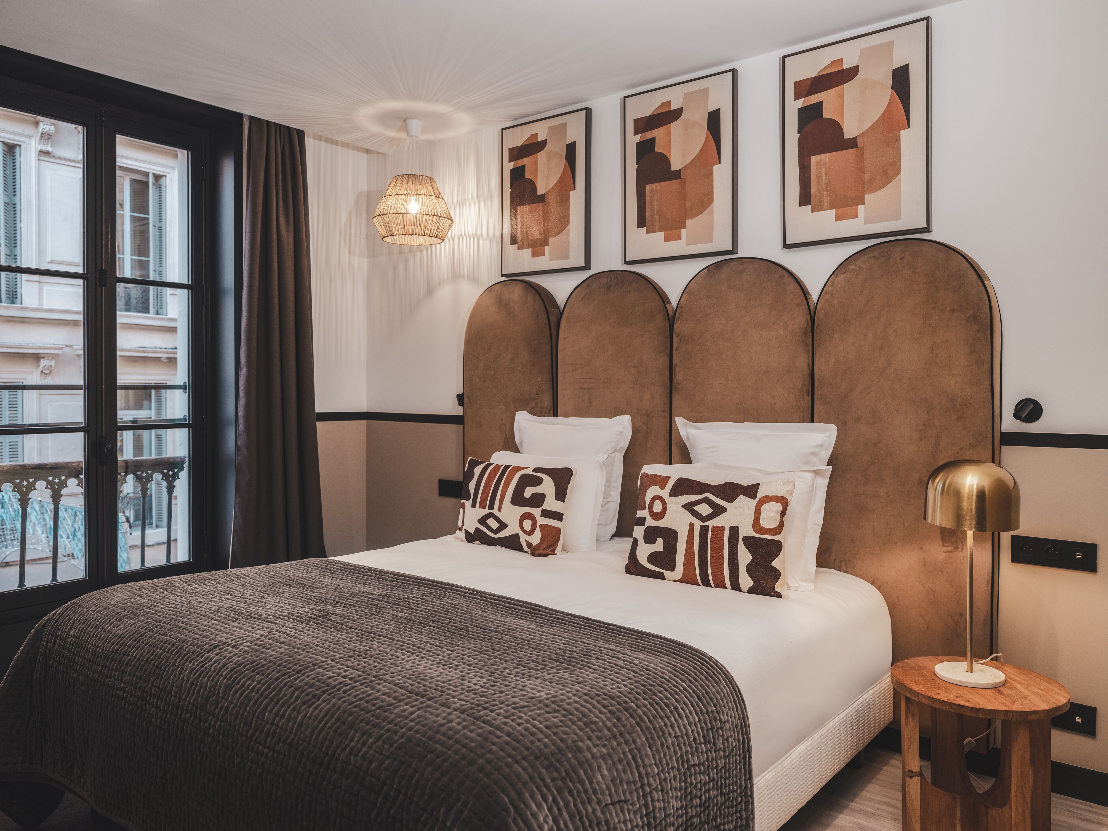 Une chambre d’hôtel moderne avec un grand lit, une tête de lit en bois et une œuvre d’art abstraite au mur.
