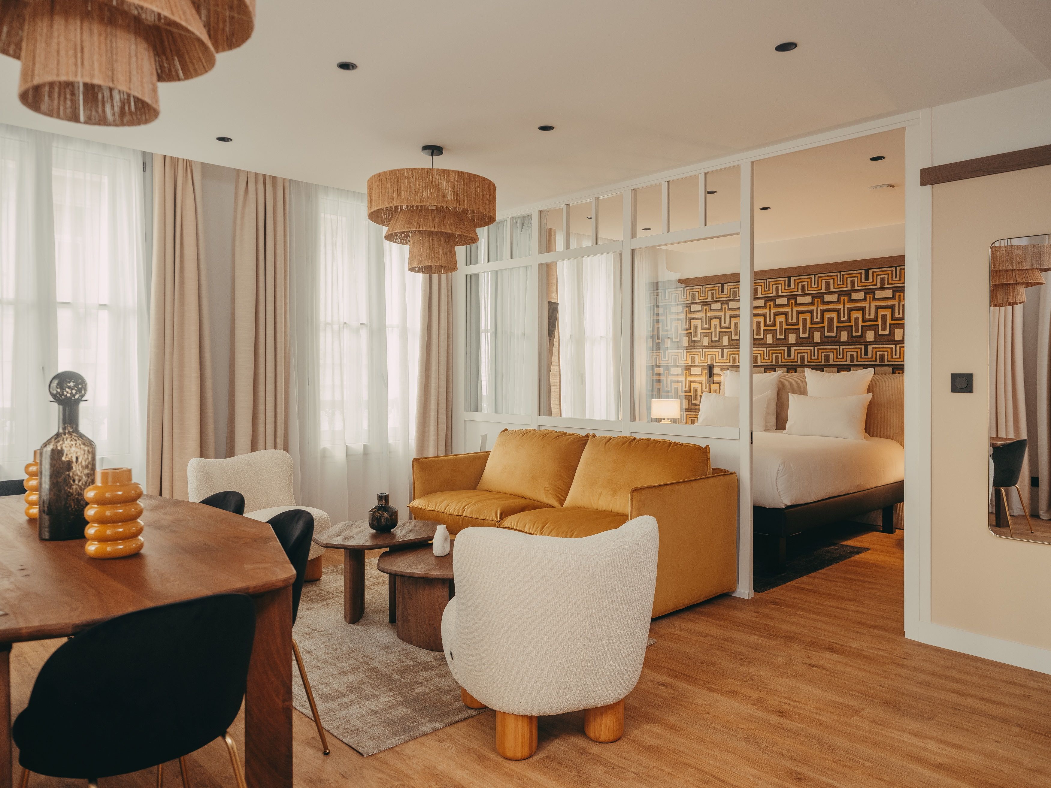 A modern hotel room with a sofa, a dining table, and a separate bedroom area.