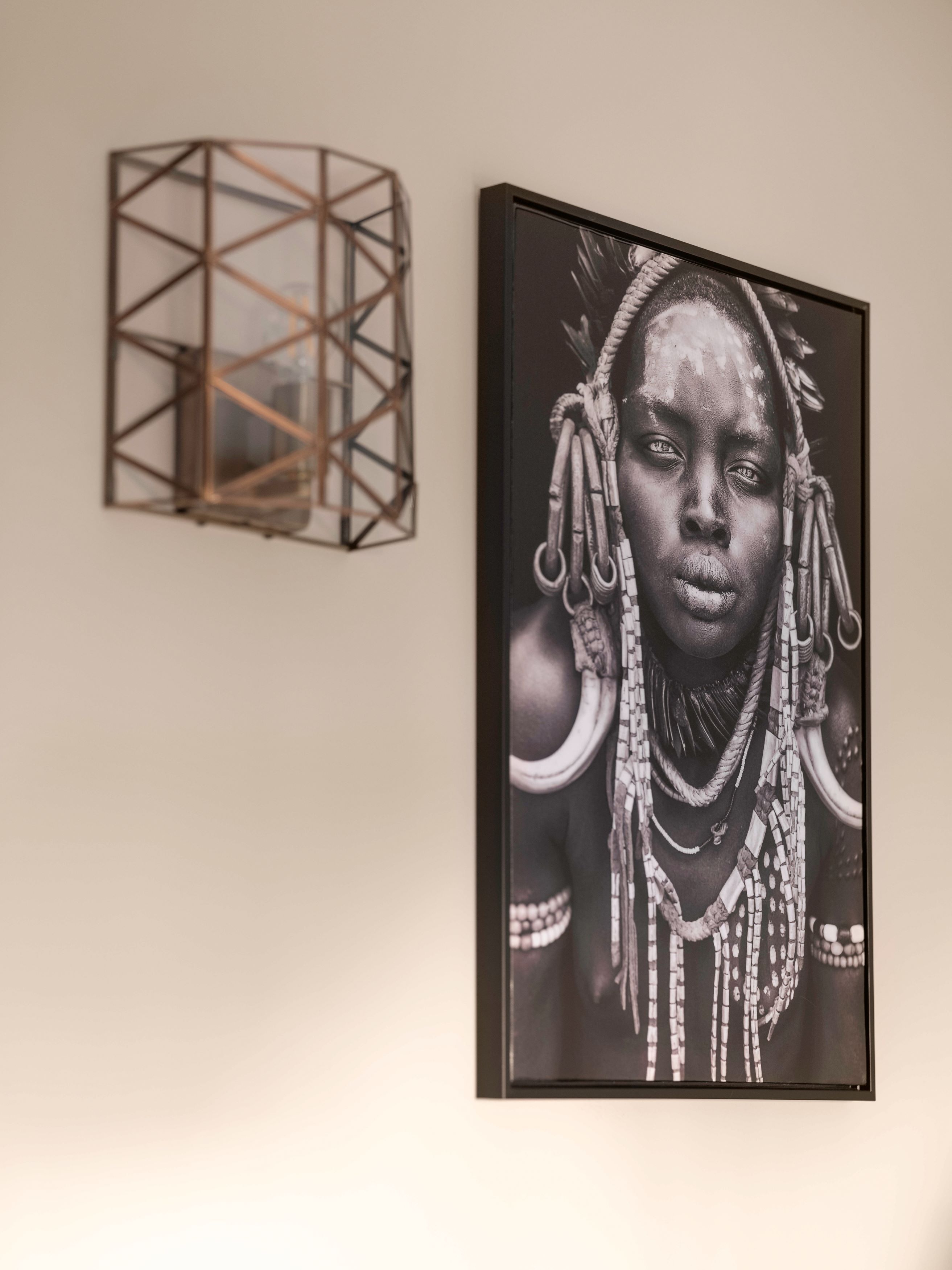 A framed black and white photograph of a person with elaborate jewelry on a wall.