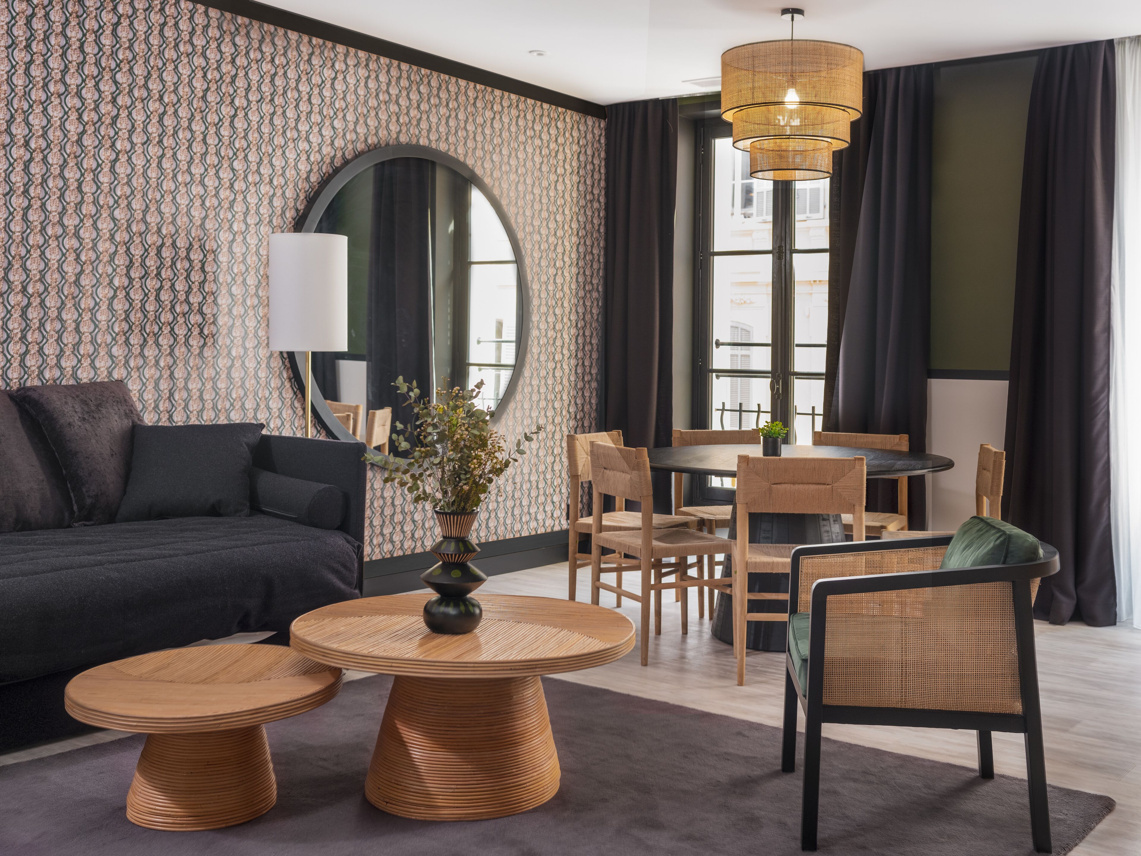 A modern living room with a sofa, two round tables, a dining table with chairs, a large mirror, and a hanging light fixture.