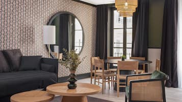 A modern living room with a sofa, two round tables, a dining table with chairs, a large mirror, and a hanging light fixture.