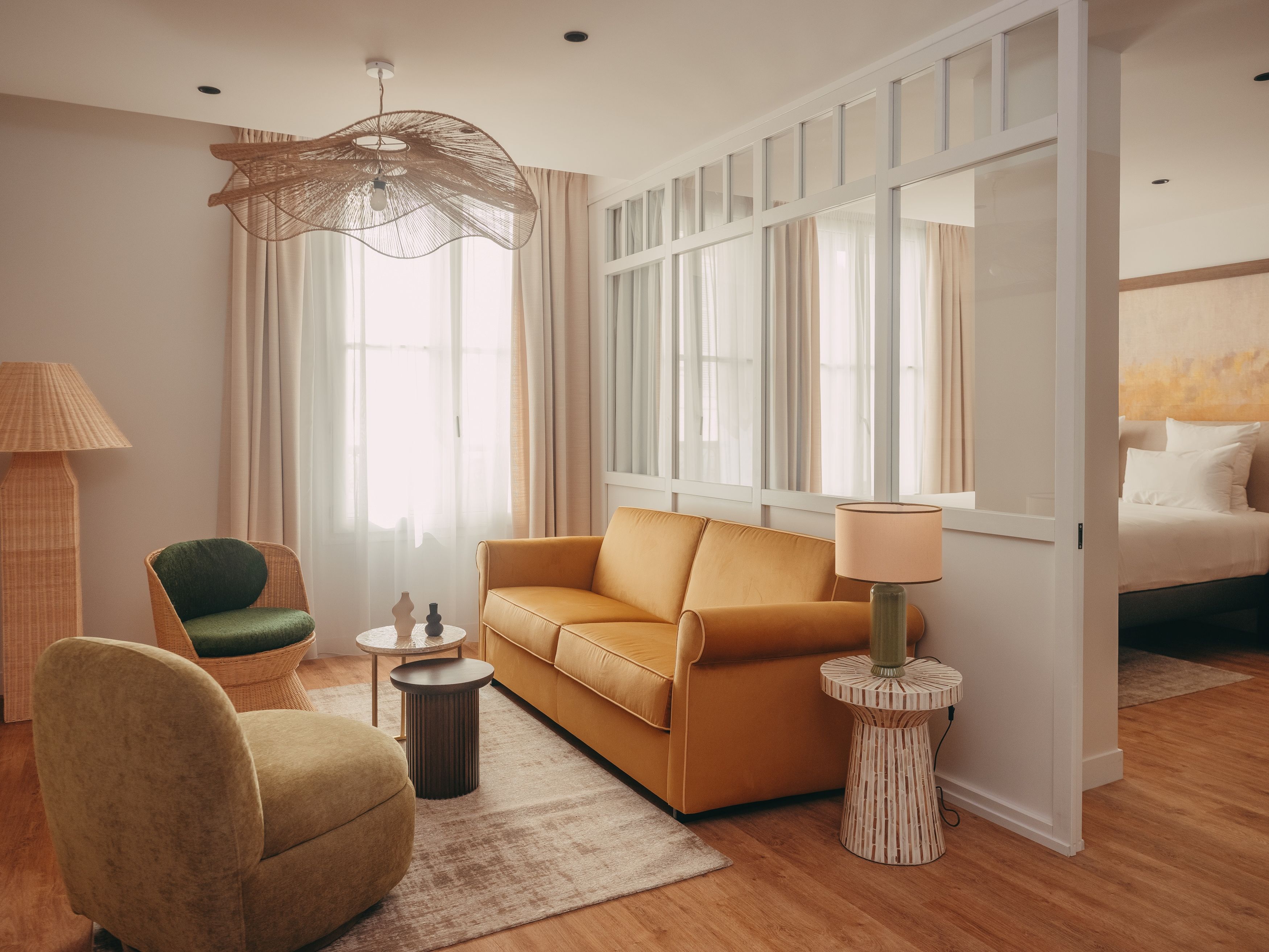 A modern living room with a sofa, armchair, lamp, and a large window with curtains.