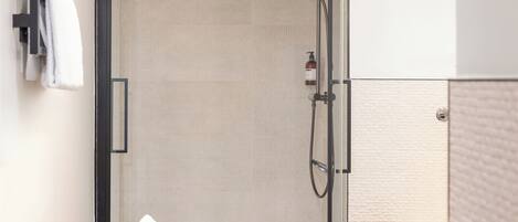 A modern bathroom with a glass-enclosed shower, a black soap dish, and a white toilet.