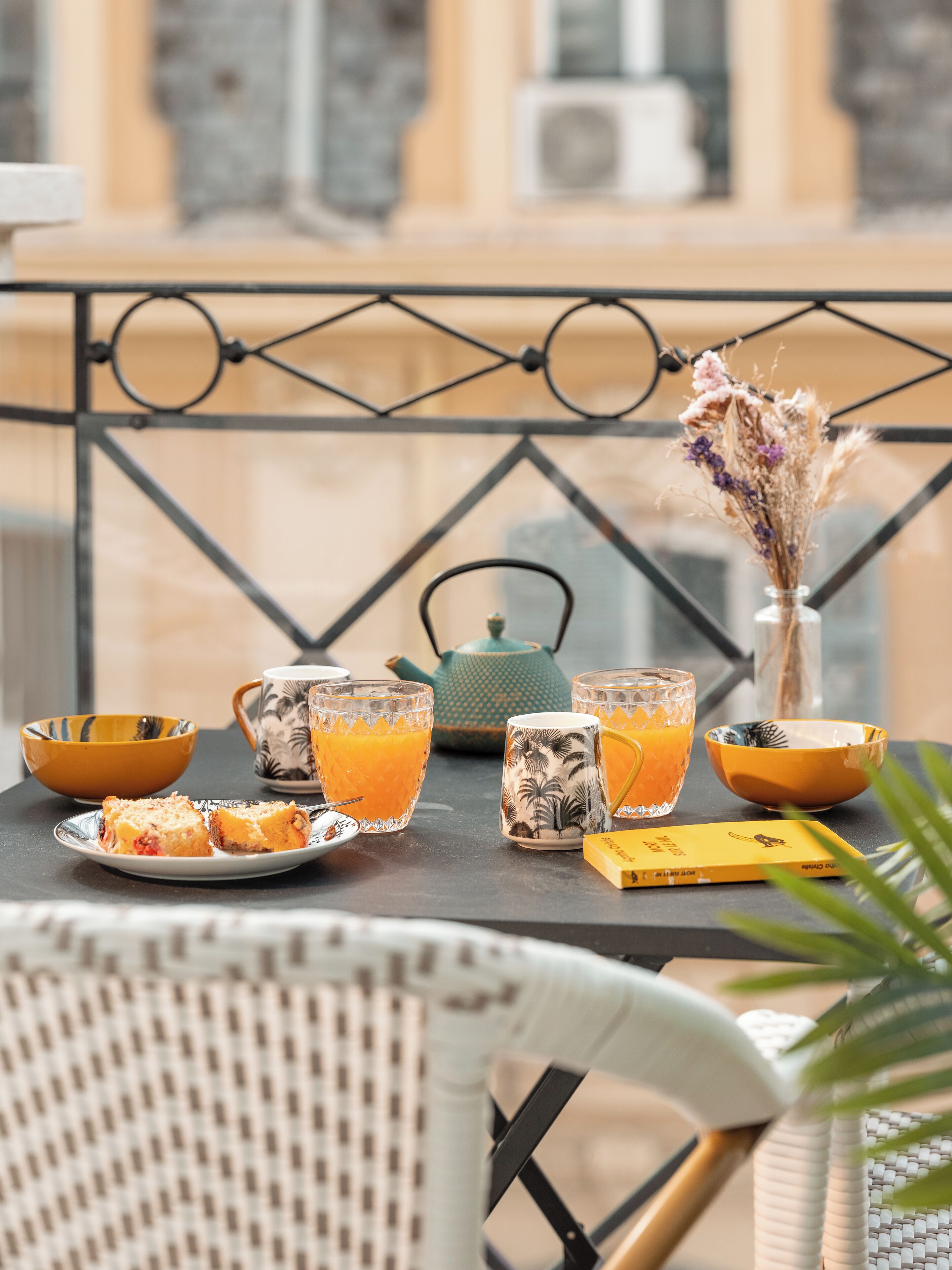 A table with a glass of orange juice, a teapot, and a vase with dried flowers.